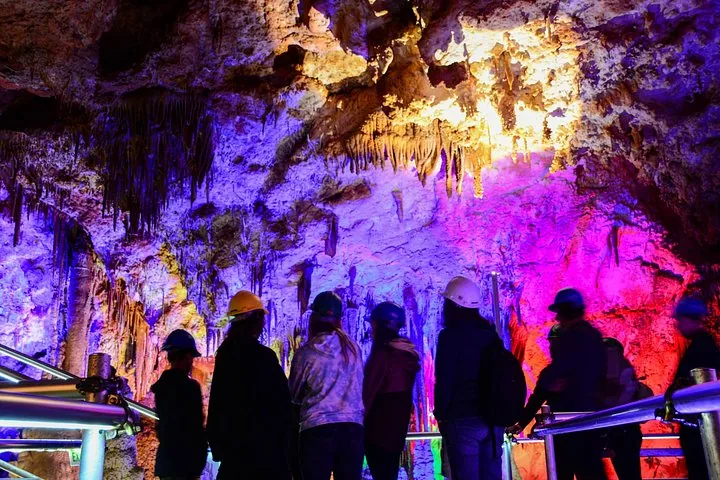 Touristen mit Schutzhelmen erkunden bunte beleuchtete Höhlenformationen