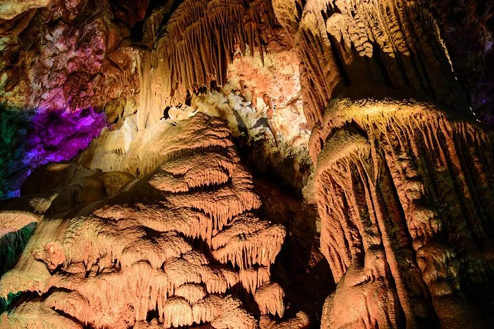 Große, kaskadenartige Höhlenformationen, beleuchtet mit warmem und farbigem Licht